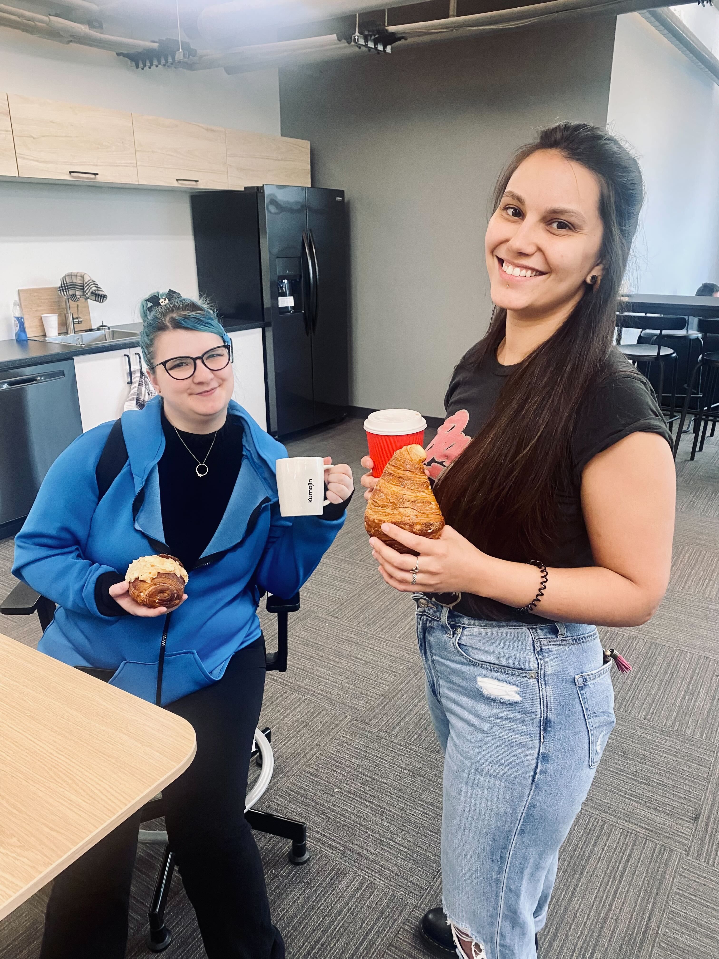 Two team members smiling with a coffee and croissant in their hands